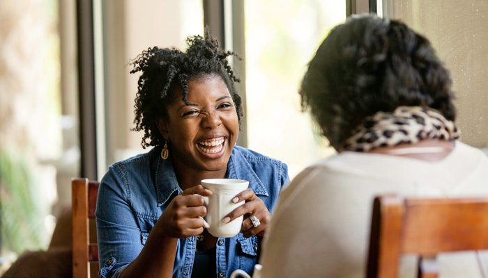 Two females catching up during a befriending session over a coffee, smiling at one another